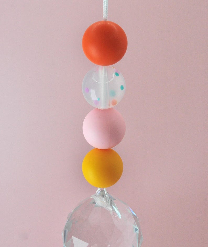 May include: A colorful beaded car charm with a crystal prism at the bottom. The beads are orange, clear with confetti, pink, and yellow.