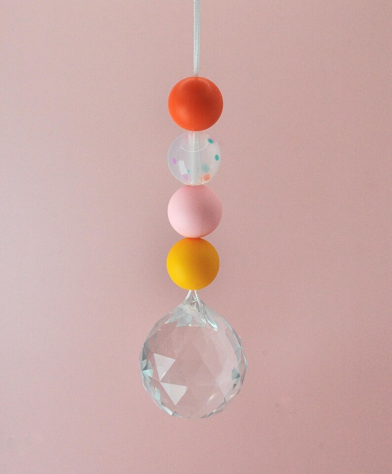 May include: A crystal suncatcher with a string of colorful beads. The beads are orange, pink, clear with confetti, and yellow.