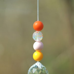 May include: A crystal suncatcher with a string of colorful beads. The beads are orange, white with colorful dots, pink, and yellow.
