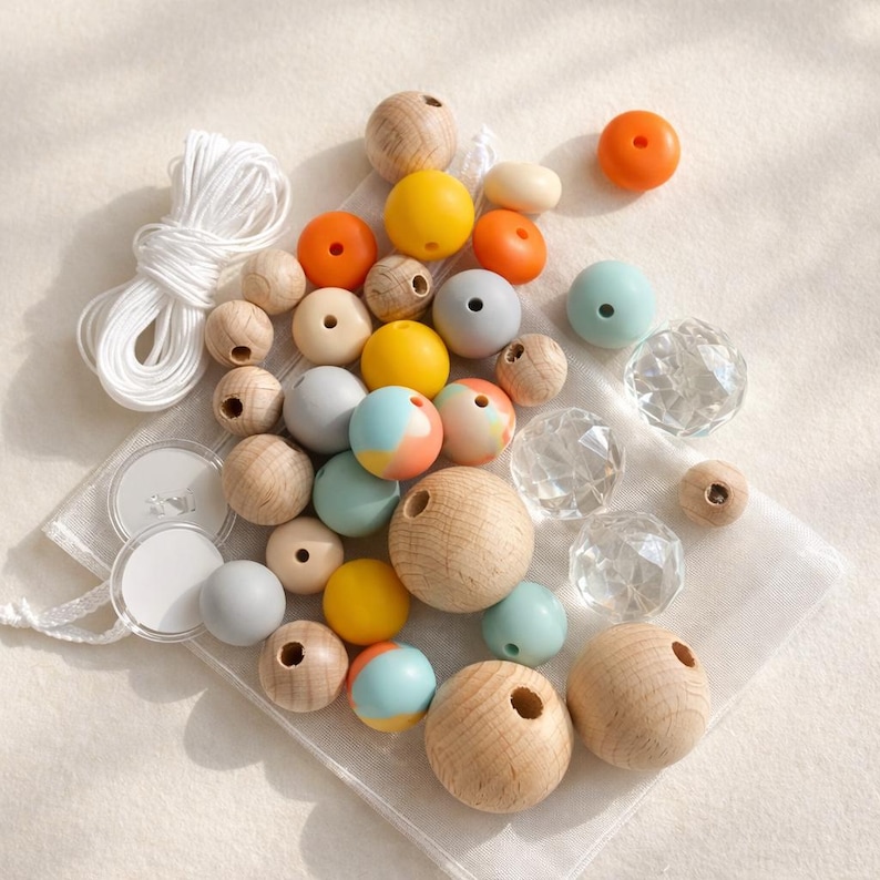 May include: A collection of craft beads in various colors and materials. The assortment includes wooden beads, clear faceted beads, and colorful silicone beads in shades of orange, yellow, and teal. White string and small clear discs are also included.
