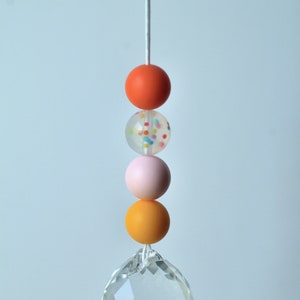 May include: A crystal suncatcher with a string of colorful beads. The beads are orange, white with colorful sprinkles, pink, and yellow.