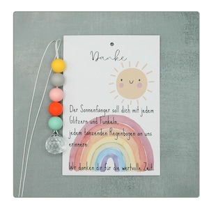 May include: A decorative card with the word "Danke" and a smiling sun illustration. The card features a rainbow and text in German. A string of colorful beads and a crystal ball hang from the card.