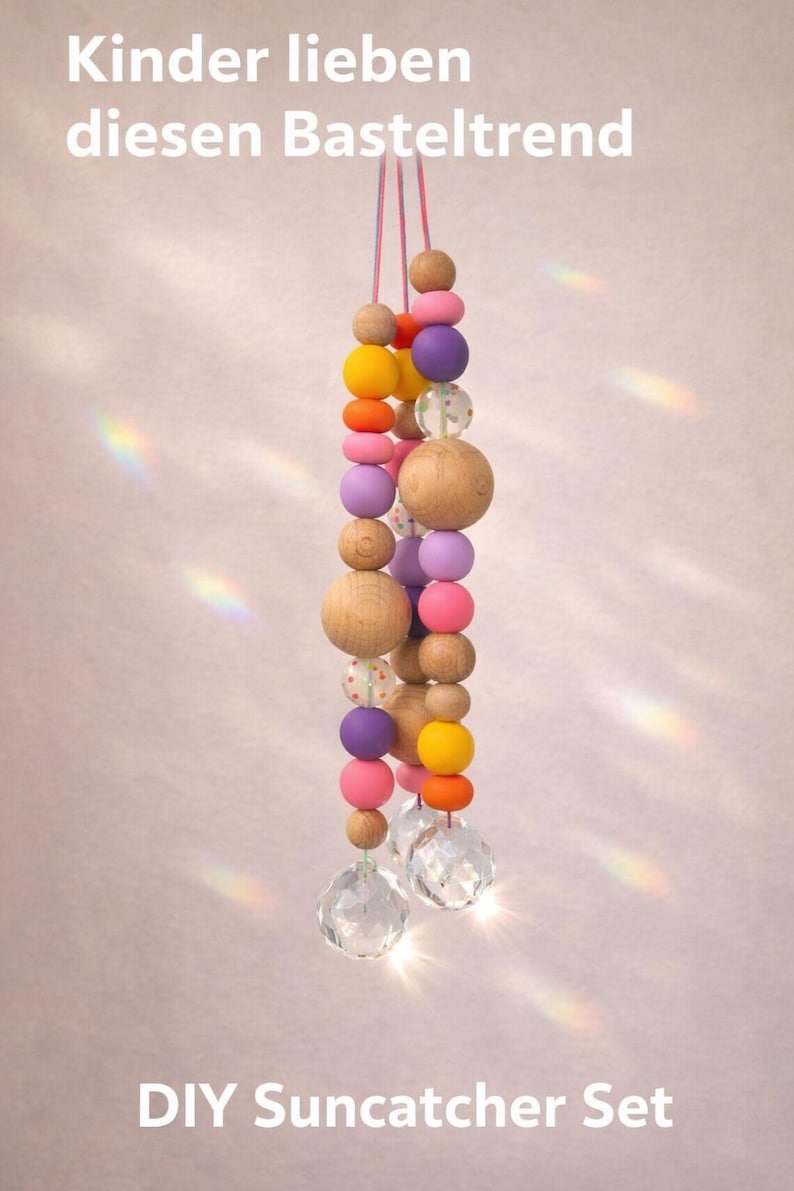 May include: A DIY suncatcher set featuring a string of colorful wooden beads in various sizes and colors, including pink, orange, yellow, and purple. The beads are strung together with a clear crystal at the bottom. Text on the image reads "Kinder lieben diesen Basteltrend".