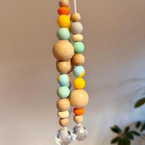 May include: Two strands of decorative beads with a variety of colors and sizes. The beads include natural wood, orange, yellow, light blue, and gray. Each strand ends with a clear, faceted crystal. The beads are strung on white cord.