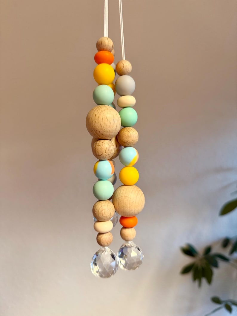 May include: Two strands of decorative beads with a variety of colors and sizes. The beads include natural wood, orange, yellow, light blue, and gray. Each strand ends with a clear, faceted crystal. The beads are strung on white cord.