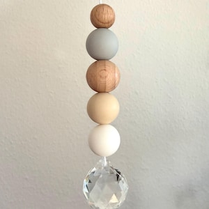 May include: A decorative hanging ornament featuring a string of wooden beads in natural wood, gray, and cream colors, culminating in a clear, faceted crystal ball. The beads are spherical and vary in size.