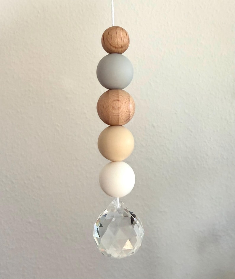 May include: A decorative hanging ornament featuring a string of wooden beads in natural wood, gray, and cream colors, culminating in a clear, faceted crystal ball. The beads are spherical and vary in size.