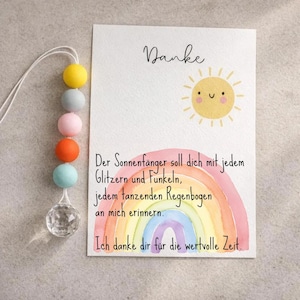 May include: A greeting card with the word "Danke" and a smiling sun illustration. The card features a watercolor rainbow and text in German. A decorative suncatcher with colorful beads and a crystal prism hangs from the top.