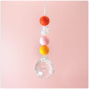 May include: A crystal suncatcher with a string of colorful beads. The beads are orange, clear with confetti, pink, and yellow.