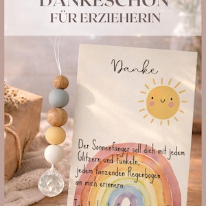 May include: A card with the text "Danke" and a watercolor rainbow and sun illustration. A string of wooden beads in various colors hangs next to the card. The text "KLEINES DANKESCH&Ouml;N F&Uuml;R ERZIEHERIN" is at the top.