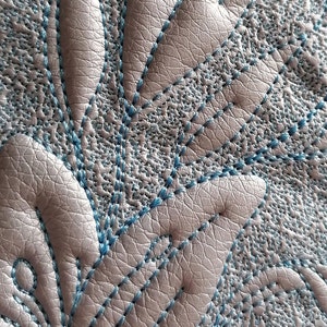 K&ouml;nnte beinhalten: Nahaufnahme einer hellgrauen Lederoberfl&auml;che mit einem blauen gestickten Blumenmuster.