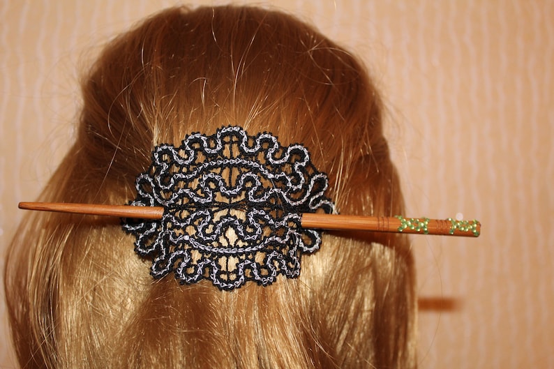 Op de afbeelding: Een zwarte en zilveren kant haar kam met een houten stok versierd met groene steentjes.