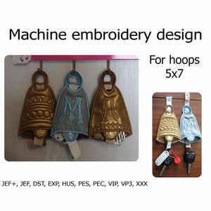 May include: Three embroidered bell-shaped keychains, one gold, one blue, and one gold with a letter H on it. The keychains are hanging on hooks. The image also shows a smaller version of the keychains hanging on hooks. The text "For hoops 5x7" is visible in the image. The text "JEF+, JEF, DST, EXP, HUS, PES, PEC, VIP, VP3, XXX" is also visible in the image.