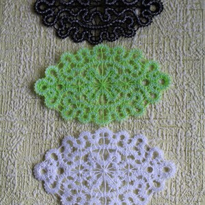 Op de afbeelding: Drie gehaakte doilies in zwart, groen en wit. De doilies zijn ovaalvormig en hebben een delicaat, ingewikkeld ontwerp.