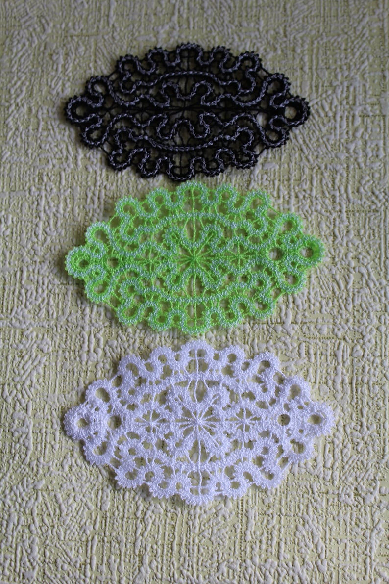 Op de afbeelding: Drie gehaakte doilies in zwart, groen en wit. De doilies zijn ovaalvormig en hebben een delicaat, ingewikkeld ontwerp.