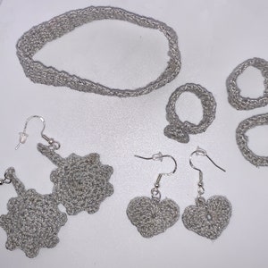 May include: A set of silver crocheted jewelry including a necklace, two pairs of earrings, and two rings.