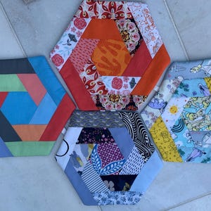 May include: Four hexagonal fabric coasters with different geometric patterns. The coasters are made of patchwork fabric in various colours, including blue, red, orange, green, and white.