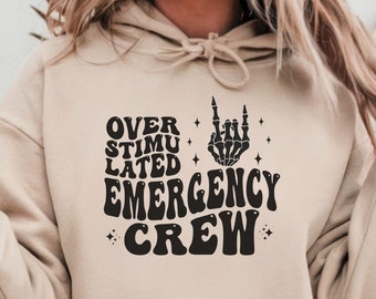 May include: A beige hoodie with a black graphic print that says "Over Stimulated Emergency Crew" with a skeleton hand making a rock and roll sign.