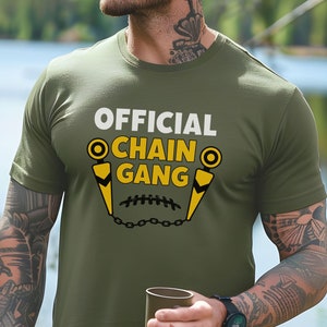 May include: A green t-shirt with the text "OFFICIAL CHAIN GANG" in white and yellow. The design features a chain and two yellow objects that resemble footballs.