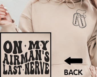 May include: A tan hoodie with a black graphic that says "On My Airman's Last Nerve" on the front and two black dog tags with the name "Jackson" on the back.