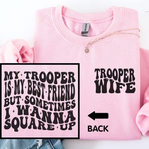 May include: A light pink sweatshirt with the words "MY TROOPER IS MY BEST FRIEND BUT SOMETIMES I WANNA SQUARE UP" in a black, retro font on the front. The back of the sweatshirt says "TROOPER WIFE" with an arrow pointing to the back.