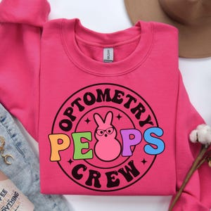 May include: Pink sweatshirt with a black and white graphic of a Peeps bunny with the text "Optometry Peeps Crew" in a circle.