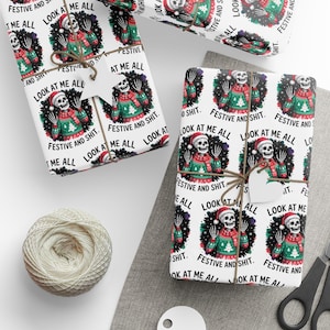 May include: White wrapping paper with a repeating pattern of a skeleton wearing a Santa hat and a Christmas sweater. The text "FESTIVE AND SHIT" and "LOOK AT ME ALL" are printed on the paper. The wrapped gifts are tied with twine.