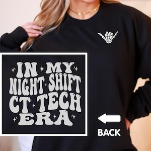 May include: Black sweatshirt with white text that reads "IN MY NIGHT SHIFT CT TECH ERA" in a retro font. A white skeleton hand in the shaka sign is on the upper right. The word "BACK" with an arrow is on the lower right.