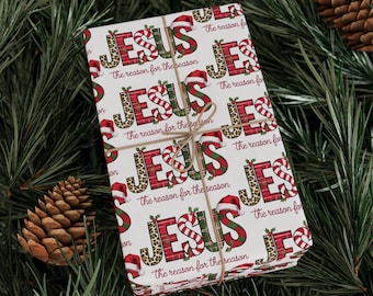 May include: A wrapped gift with a festive Christmas theme. The wrapping paper is white with the word "JESUS" in red, green, and leopard print, along with Santa hats and candy cane stripes. The gift is tied with twine.