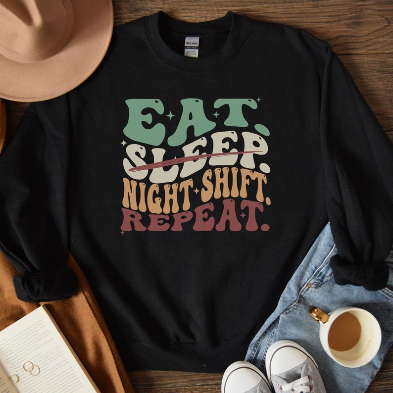 Puede incluir: Sudadera negra con un gr&aacute;fico de estilo retro que dice "Comer. Dormir. Turno de noche. Repetir."