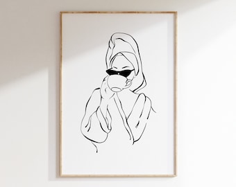 Puede incluir: Una impresión de arte lineal en blanco y negro dentro de un marco de madera clara. La ilustración muestra una figura con albornoz y una toalla envuelta en la cabeza, usando gafas de sol oscuras mientras sostiene una taza redonda para beber.