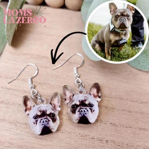 May include: A pair of dangle earrings featuring custom printed portraits of a French Bulldog. Each earring has a silver-toned metal hook and a jump ring connecting to a flat, detailed image of the dog's face. The design captures the dog's ears, eyes, and snout in a realistic color print.