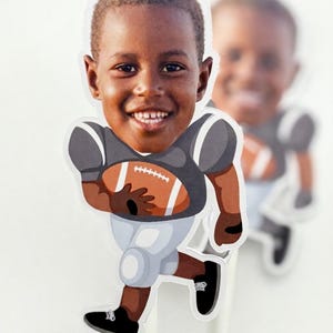 May include: A custom cake topper featuring a die-cut illustration of a smiling child with a photographic face. The character wears a gray football jersey, light gray pants, and black shoes, while holding a brown football with white laces.