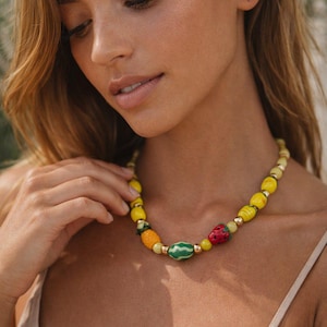 May include: A colorful beaded necklace featuring fruit-shaped beads. The necklace includes beads shaped like a strawberry, watermelon, and pineapple, interspersed with yellow and gold beads. The necklace is a vibrant accessory.