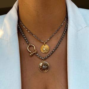 May include: Two gold necklaces with a silver chain. The top necklace has a gold coin pendant featuring a woman's face. The bottom necklace has a gold coin pendant with a compass design.