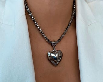 May include: A silver chain necklace with a large, silver heart pendant.