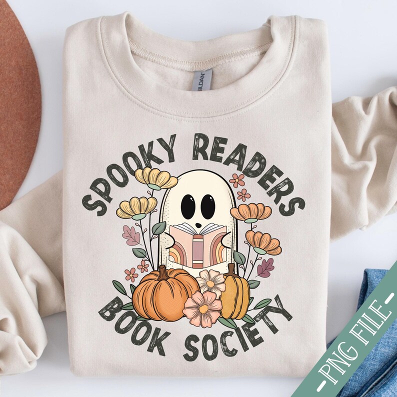 Pode incluir: Uma camisa de moletom bege com o texto "Spooky Readers Book Society" em letras pretas. Um fantasma de desenho animado est&aacute; segurando um livro e est&aacute; cercado por flores e ab&oacute;boras.