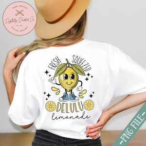 Pu&ograve; includere: Maglietta bianca con una grafica di un limone di cartone animato con un viso sorridente e il testo "Fresh Squeezed Delulu Lemonade".