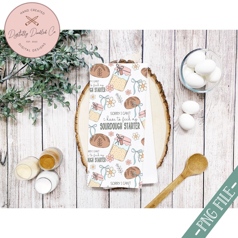 May include: A white kitchen towel with a repeating pattern of jars of sourdough starter, loaves of bread, and flowers. The text on the towel reads "Sorry I can't I have to feed my sourdough starter".