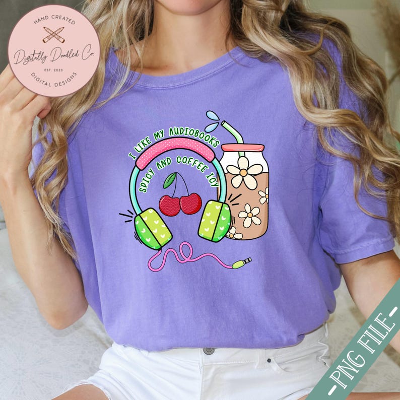 May include: Purple t-shirt with a graphic design of headphones, cherries, and a glass of iced coffee. The text on the graphic says "I like my audiobooks spicy and coffee icy".