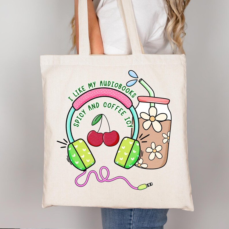 May include: A white tote bag with a colorful graphic design featuring headphones, cherries, and a glass of iced coffee. The text on the bag reads "I like my audiobooks spicy and coffee icy."