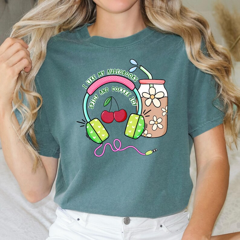 May include: Teal t-shirt with a graphic design of headphones, cherries, and a glass of iced coffee. The text on the shirt reads "I like my audiobooks spicy and coffee icy."