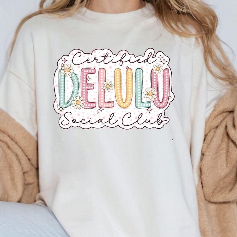May include: A white sweatshirt with a graphic design that says "Certified Delulu Social Club" in a colorful, retro-inspired font with flowers and stars.