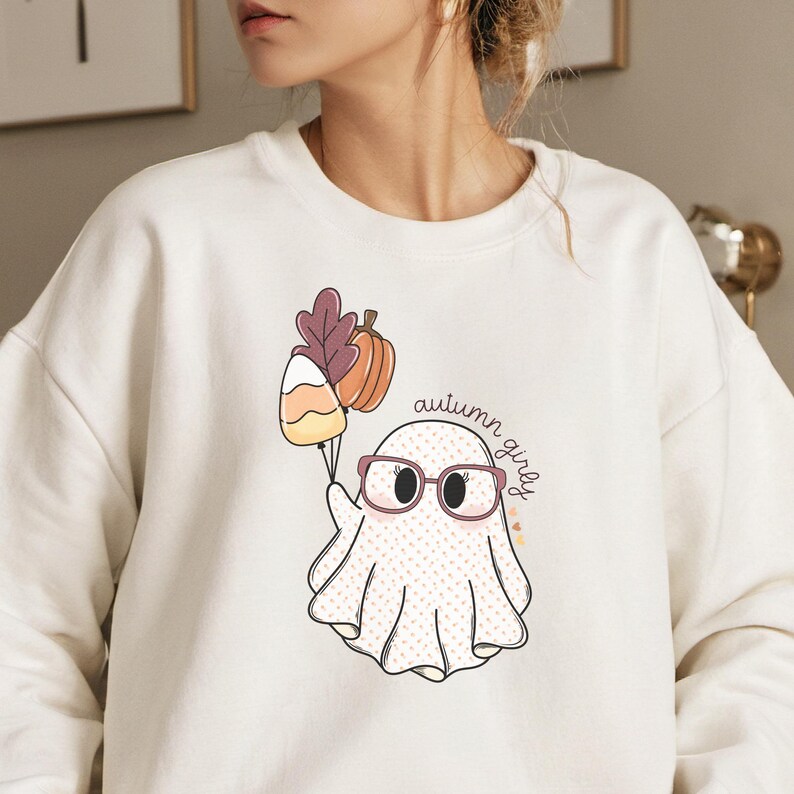 May include: White sweatshirt featuring a cute ghost wearing glasses and holding a candy corn, a pumpkin, and autumn leaves. The text "autumn girls" is written on the sweatshirt.