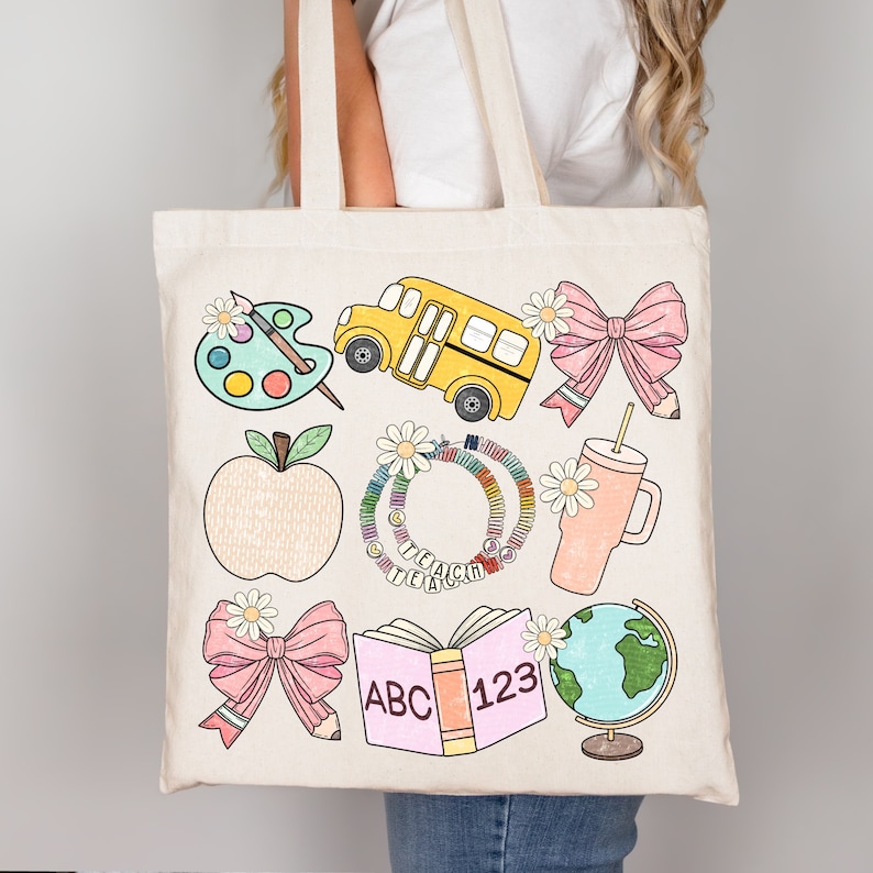 May include: A beige tote bag featuring colorful illustrations of school-related items. The design includes a yellow school bus, a palette with paint, a pink bow with a pencil, an apple, a bracelet with the word TEACH, a pink tumbler, an open book with ABC 123, and a globe.