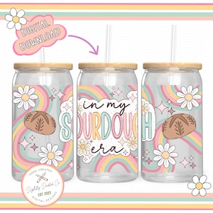 May include: Three clear glass tumblers with lids and straws. The tumblers have a rainbow design with white daisies and stars. The middle tumbler has the text "in my sourdough era" in white letters.
