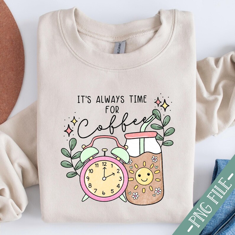 May include: A beige sweatshirt with the text "It's always time for coffee" in black lettering. A cartoon illustration of a coffee mug with a smiling sun face and a pink alarm clock with a green hand pointing to 11 o'clock.