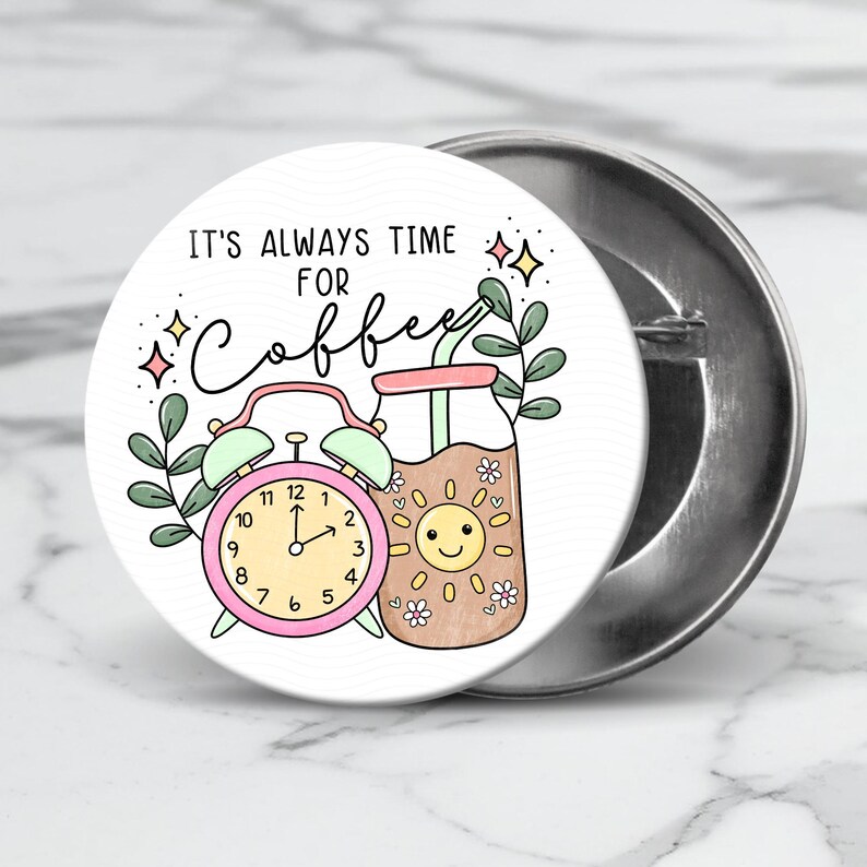May include: A white button with a pink alarm clock and a brown glass of coffee with a straw. The text on the button reads "It's always time for coffee".