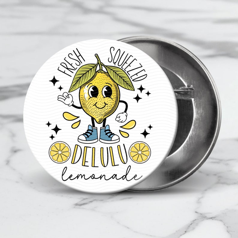 Pu&ograve; includere: Un bottone bianco con un limone di cartone animato che indossa scarpe da ginnastica blu e il testo "Fresh Squeezed Delulu Lemonade".