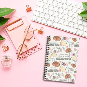 May include: A white spiral bound notebook with a cute illustration of a sourdough starter and bread. The notebook has a repeating pattern of the illustration and the text "Sorry I can't I have to feed my sourdough starter".